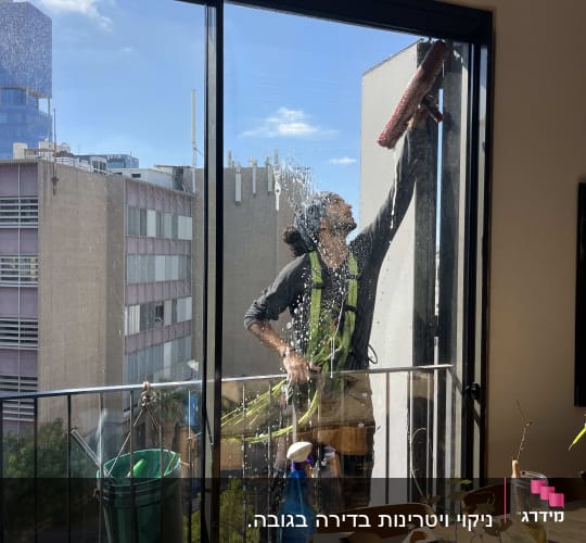 אדם מנקה חלון מבחוץ עם מגב ודלי ירוק